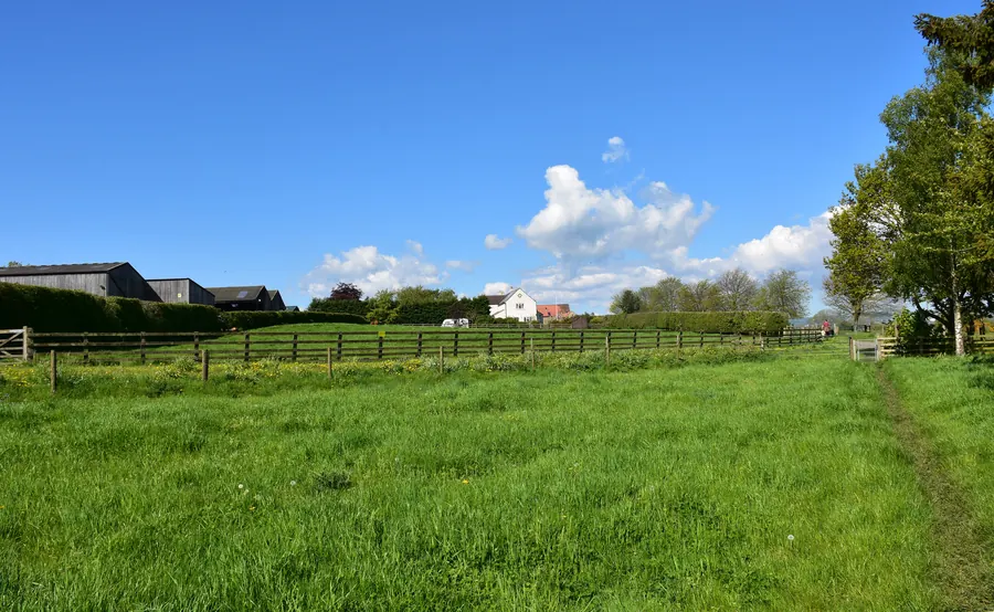 Terrain à bâtir plat, haies bocagères, quelques maisons au loin
