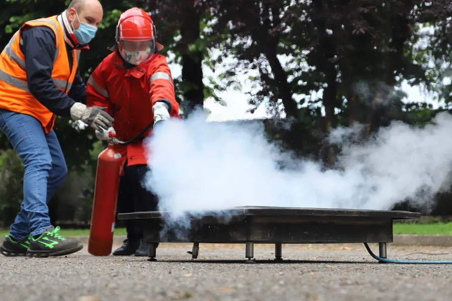 Salariée qui éteint un feu au bac avec un extincteur, formateur à côté
