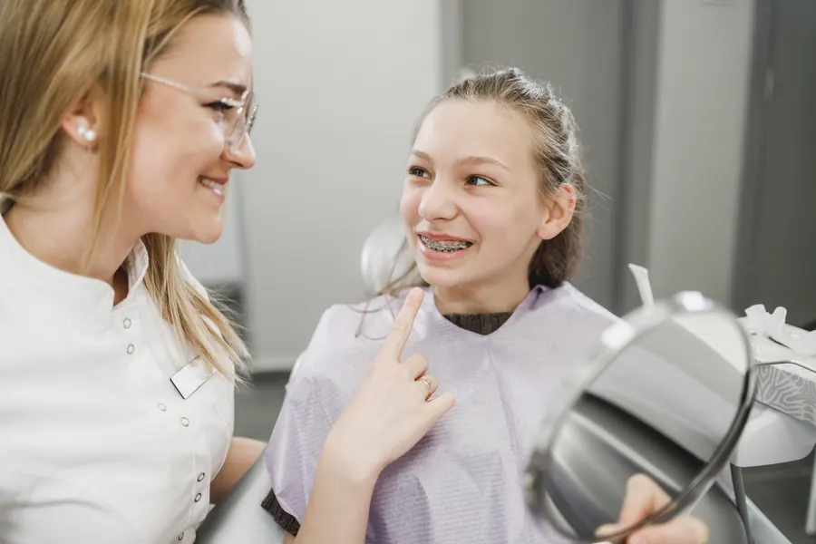 Adolescente avec des bagues, assise au fauteuil, qui échange en souriant avec la praticienne, ambiance claire et colorée