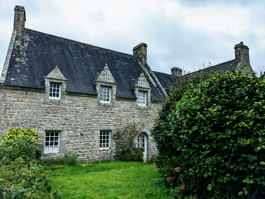 Longère en pierre avec toit d'ardoise entourée de verdure, sans fumée de cheminée