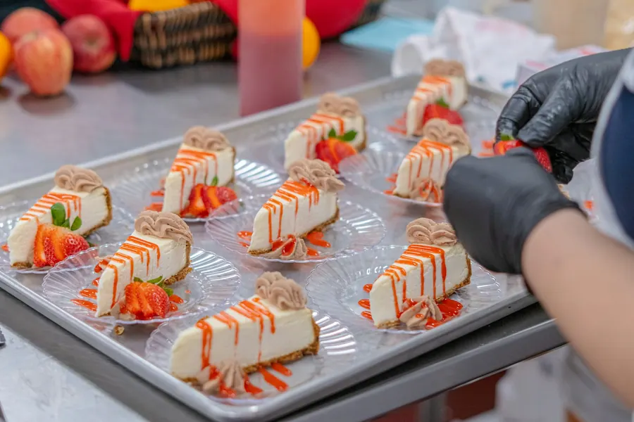 Mains gantées qui décorent des parts de cheesecake au coulis