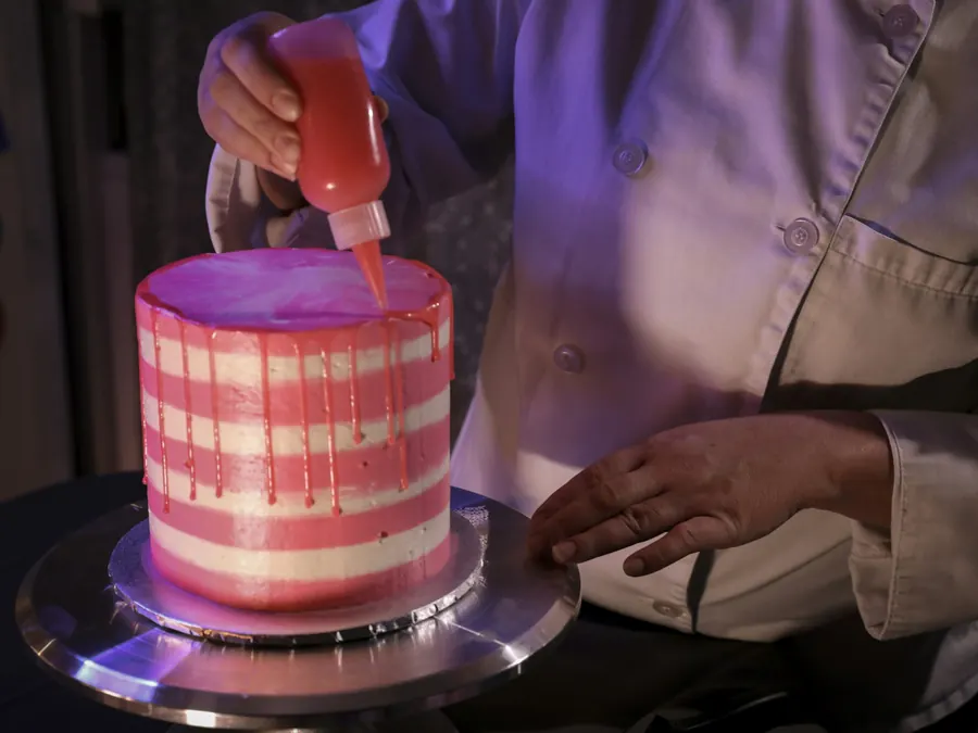 Pâtissier qui dépose un glaçage coulant sur un gâteau rose à rayures
