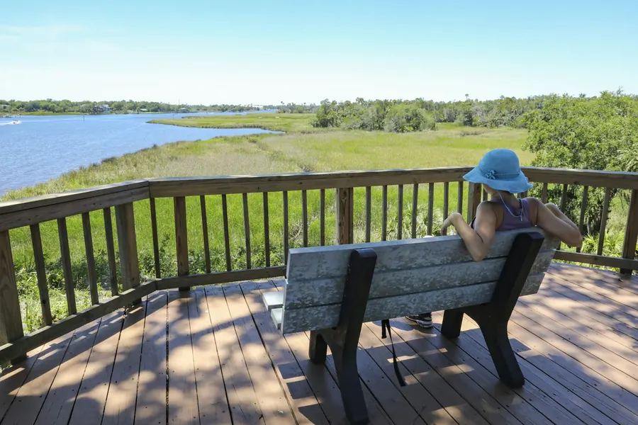Terrasse en bois naturel bordée de graminées, rivière en contrebas