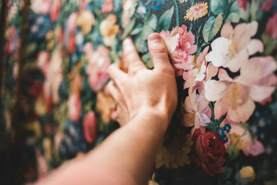 Main qui lisse un papier peint fleuri, sans brosse visible