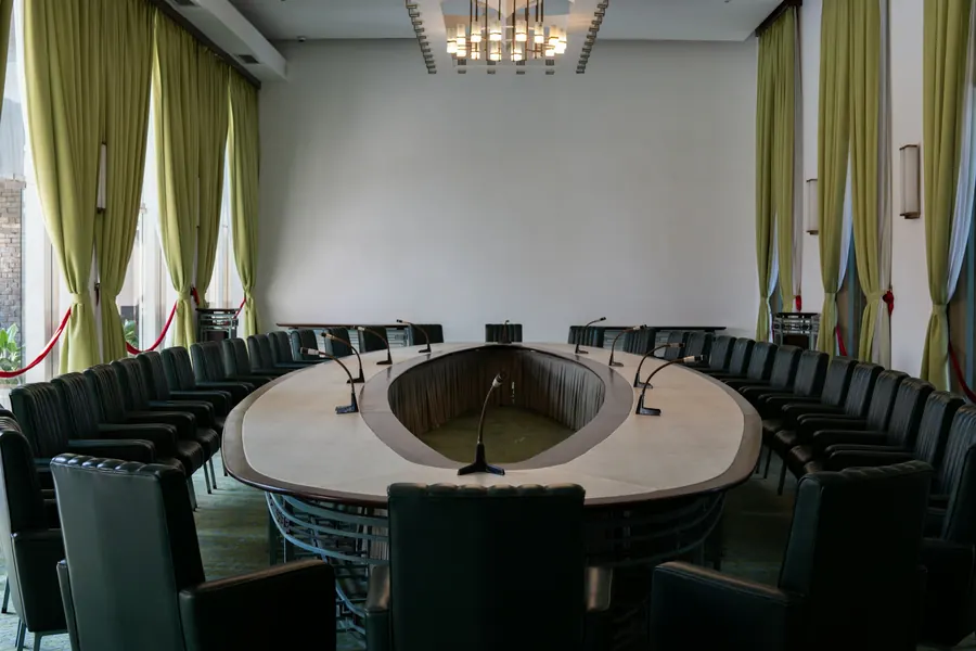 Salle de conseil en fer à cheval avec micros, chaises vides, sans public visible