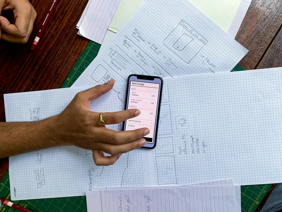 Main tenant un téléphone au-dessus de plans techniques sur table en bois