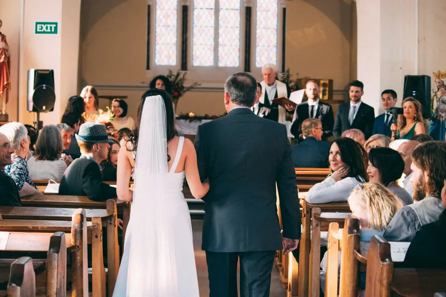 Mariée avançant dans l'allée au bras de son père, invités assis sur les bancs