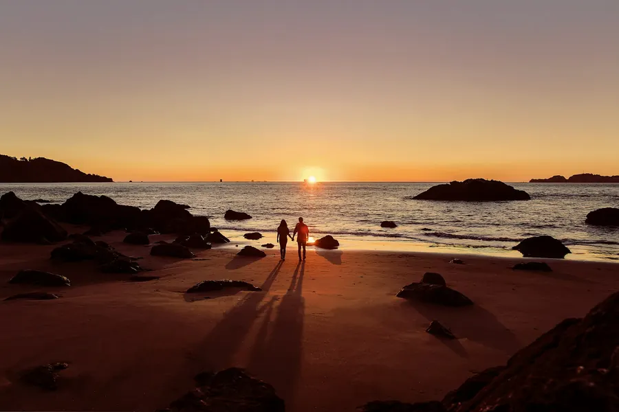 Couple enlacé sur une plage rocheuse silhouetté au coucher du soleil