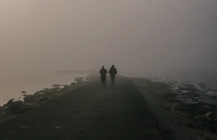 Couple en silhouette marchant dans le brouillard sur une jetée d'hiver