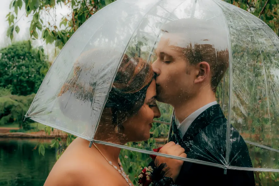 Mariés sous un parapluie transparent dans un jardin, sans chapelle ni pluie visible