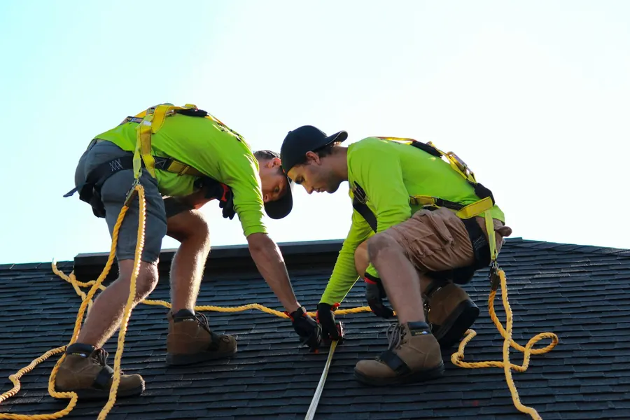 Deux poseurs harnachés sur un toit, sans panneau solaire visible