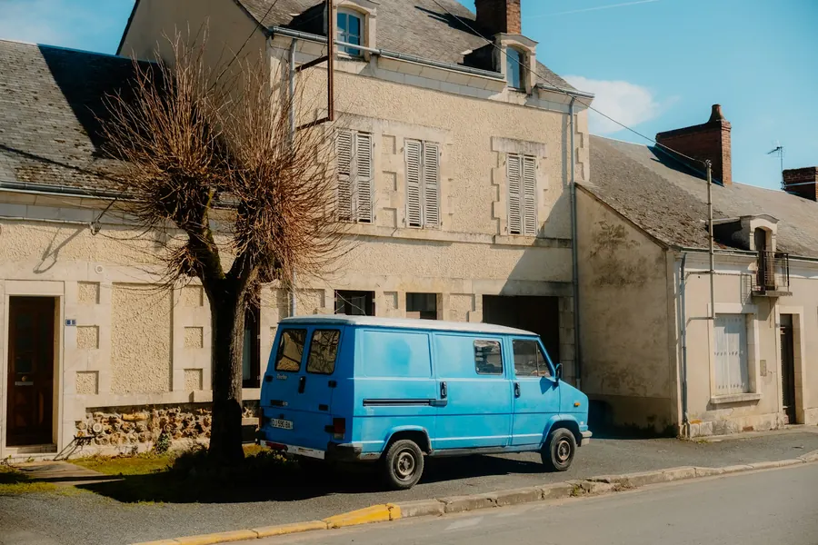 Camionnette bleue garée devant une maison en pierre à volets