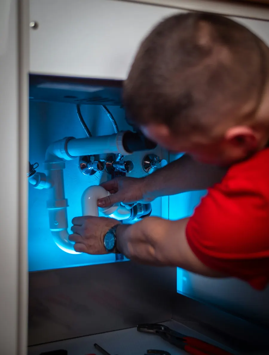 Plombier qui répare des tuyaux sous un lavabo, éclairage bleuté