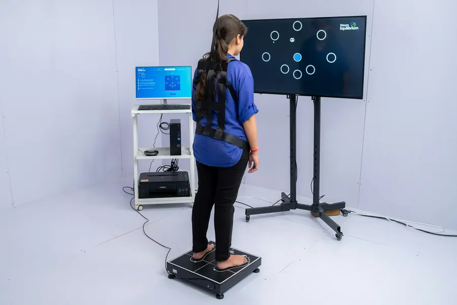 Patient debout sur une plateforme de mesure d'appui, écran en arrière-plan