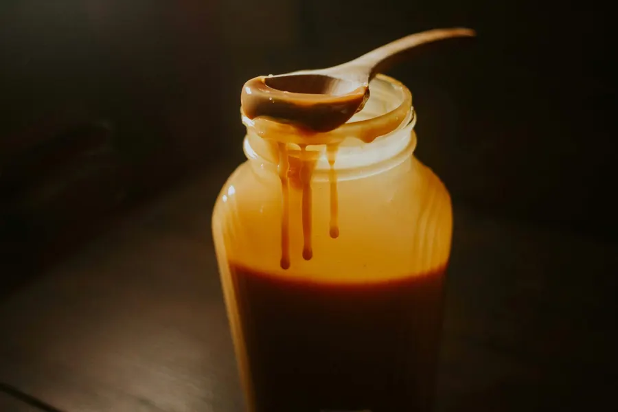 Bocal de confiture de lait ouvert, cuillère nappée qui déborde sur le verre