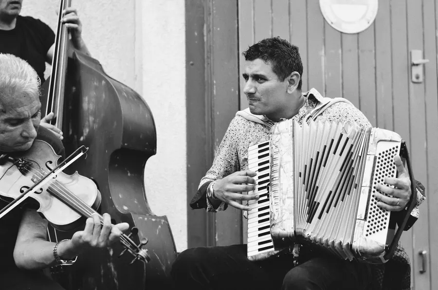 Trio de musiciens avec accordéon et contrebasse sur un porche, pas de scène visible