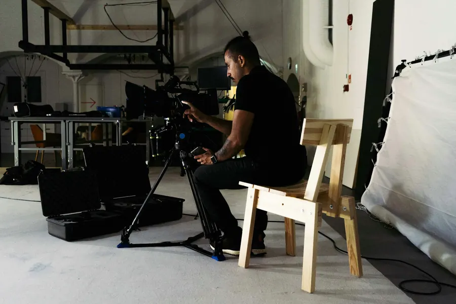 Ouvrier qui assemble une chaise de bureau, caméra sur trépied au premier plan
