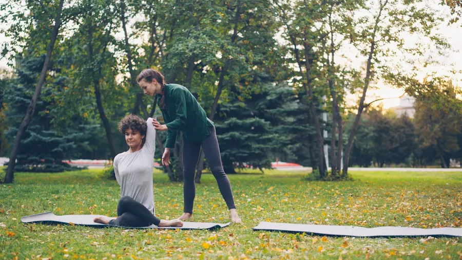 Professeure de yoga qui ajuste une élève en extérieur, sans brique visible