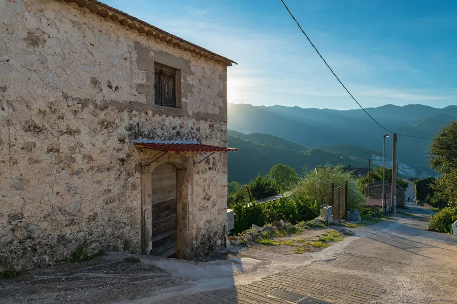 Vieux bâtiment en pierre avec chemin et collines dorées, sans vignes visibles