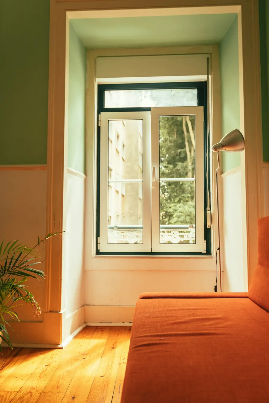 Grande fenêtre d'un appartement ancien, lumière douce, plantes, toits en fond