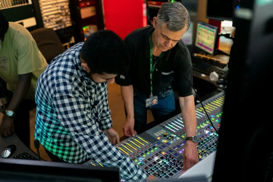 Jeune bénévole qui apprend la console de mixage avec un technicien