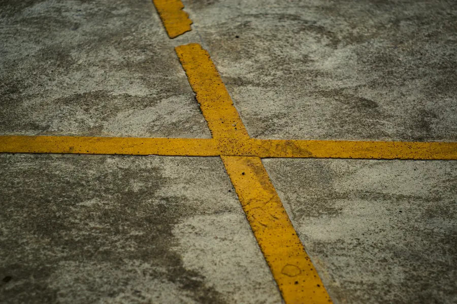 Croix jaune peinte sur une surface extérieure, sans carrelage ni mètre visible