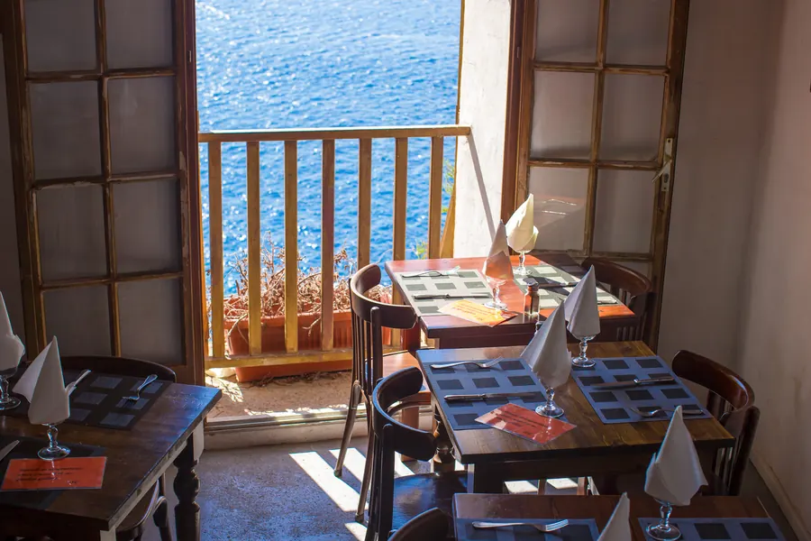 Petite salle de restaurant, tables en bois, grandes fenêtres sur le port, lumière chaude