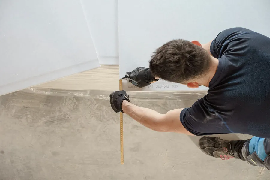 Poseur agenouillé qui mesure une latte de parquet au sol