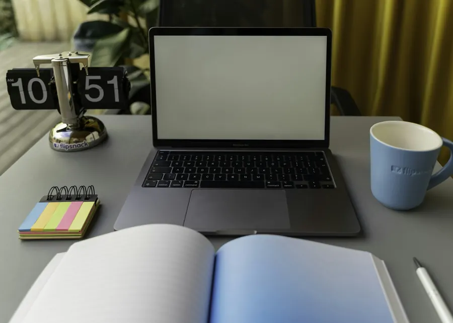 Ordinateur portable ouvert sur un bureau, livre ouvert et tasse à côté