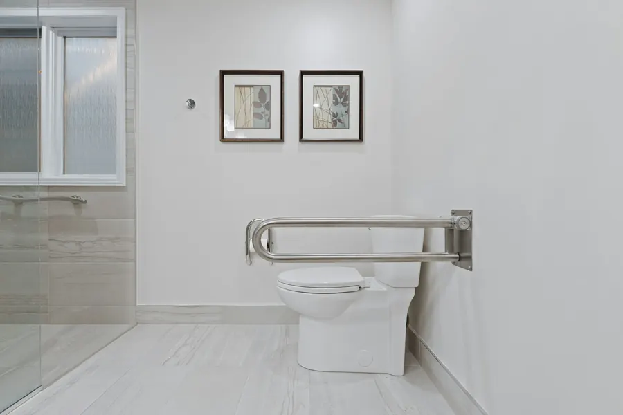 Toilettes avec barre d'appui murale et sol carrelé clair