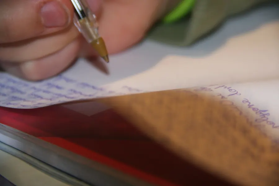 Main qui écrit au stylo sur une feuille de cahier