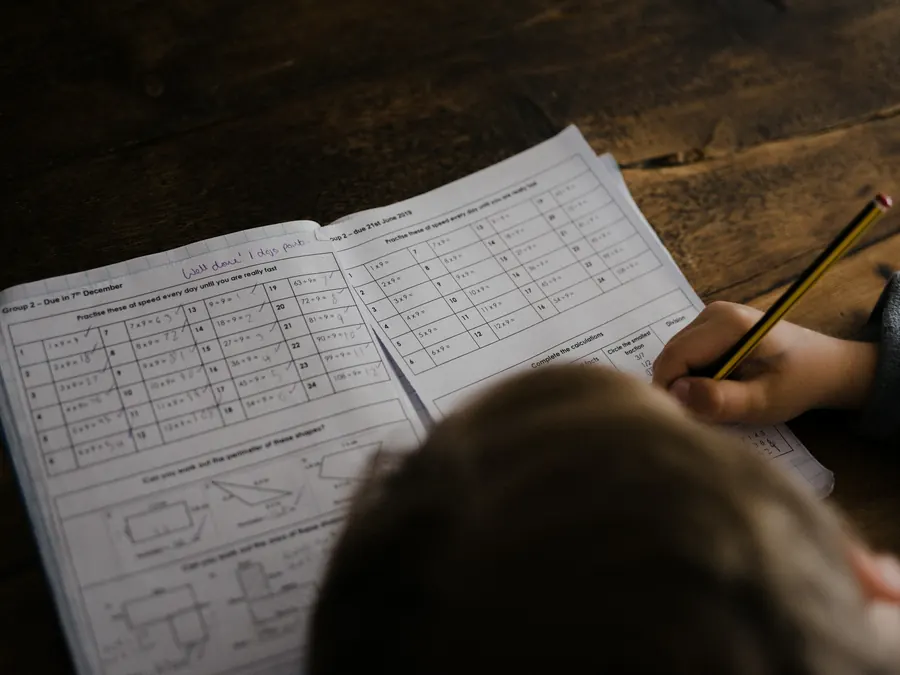 Élève vu de dos qui écrit dans son cahier d'exercices, à son bureau