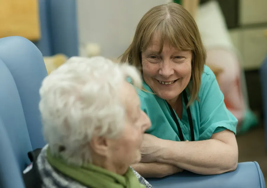 Aide-soignante souriante assise à côté d'une dame âgée