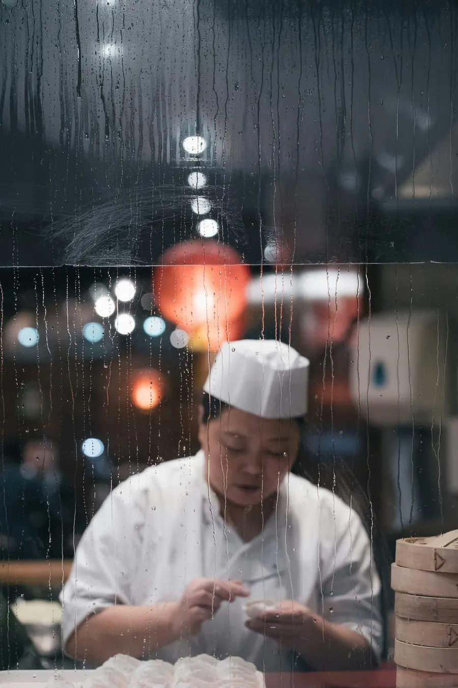 Cheffe en toque debout dans une cuisine, vue à travers une vitre