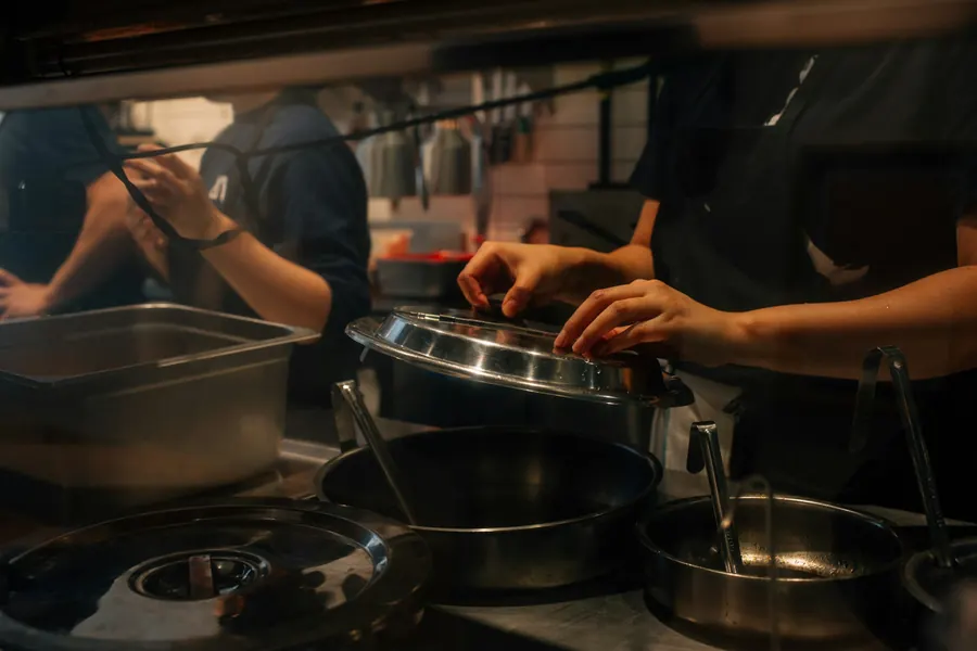 Mains de cuisiniers qui manipulent casseroles et bacs inox dans une cuisine de restaurant
