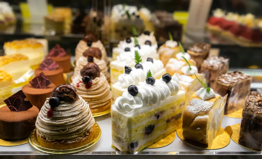 Vitrine réfrigérée de pâtisserie, entremets alignés, lumière d'après-midi