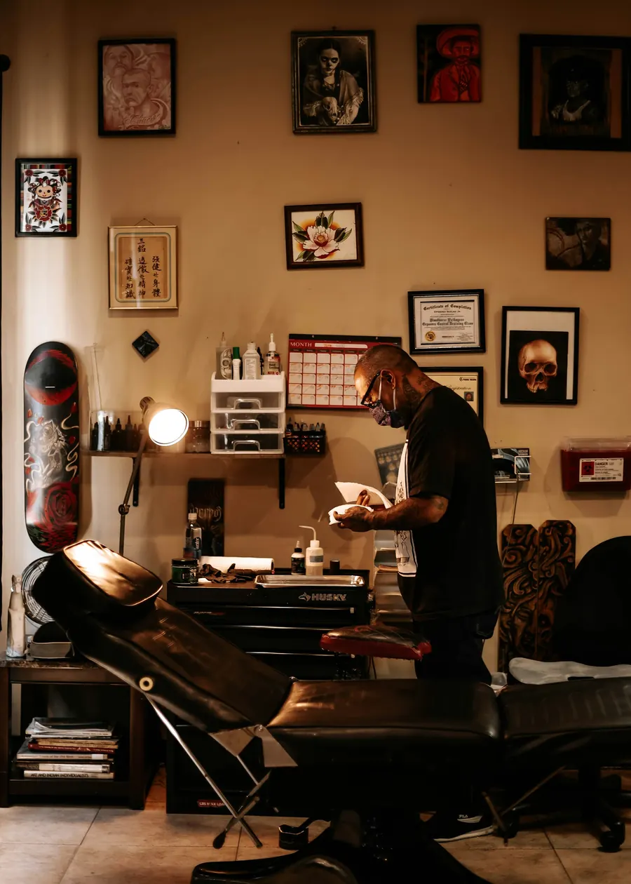 Tatoueur debout dans son studio, murs couverts de cadres et de dessins