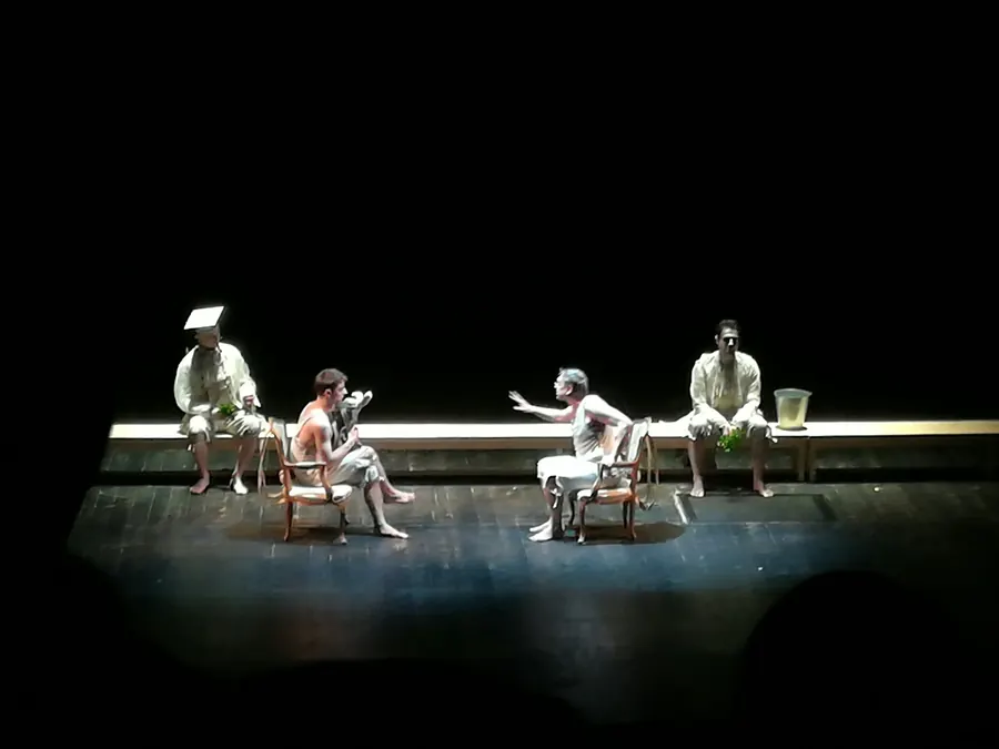 Comédiens en pleine représentation sur une scène nue, assis sur des chaises