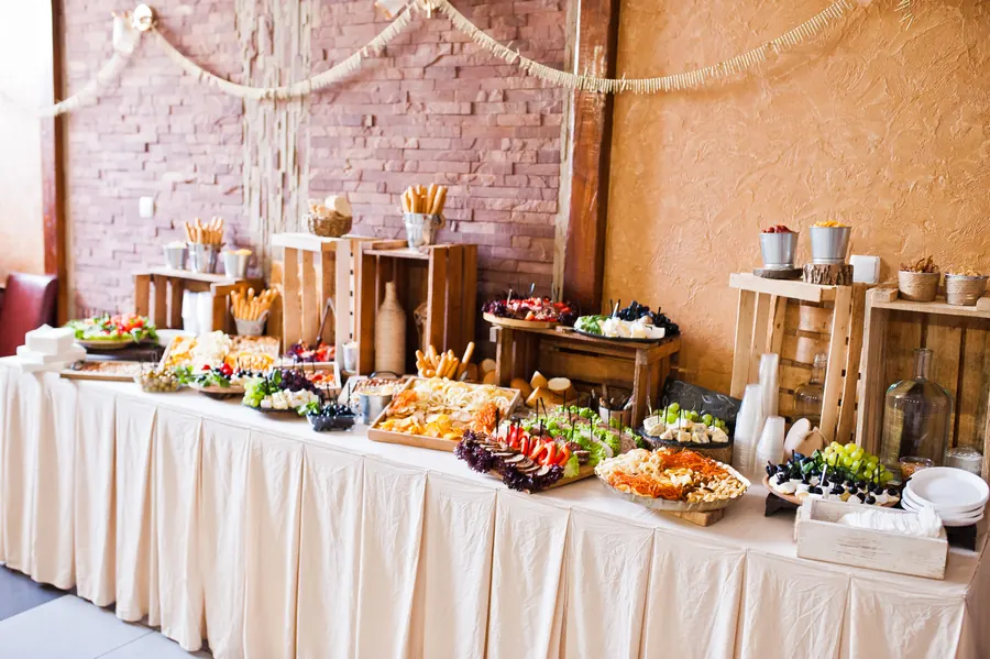 Buffet de réception dressé sur nappe en lin, plats de saison, bougies, grange en pierre