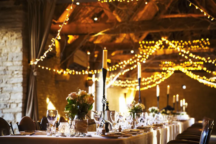 Longues tables de mariage dressées sous une charpente, bougies, verrerie