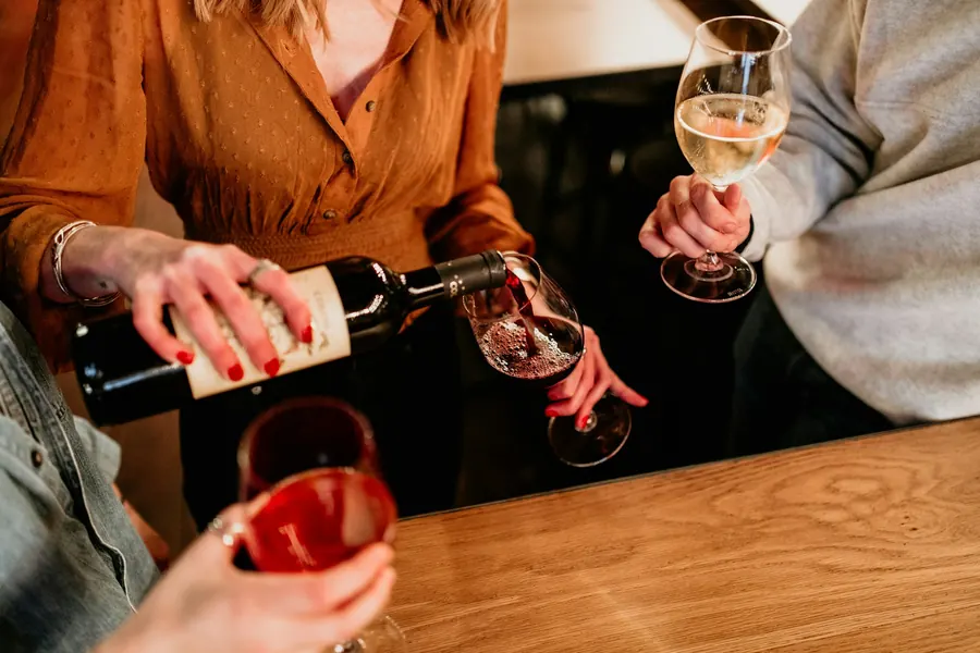 Vigneronne qui sert un fond de verre au comptoir du caveau, visiteurs de dos ou hors champ