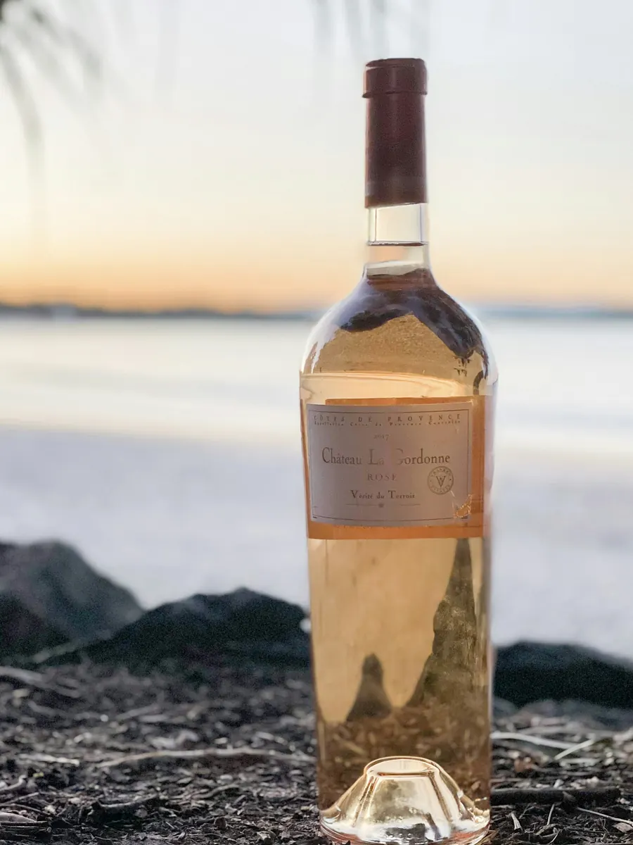 Bouteille de rosé posée sur des rochers au bord de mer, au coucher du soleil