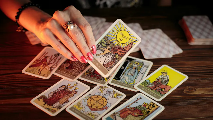 Main posée sur un tirage de cartes de tarot illustrées, sur une table en bois