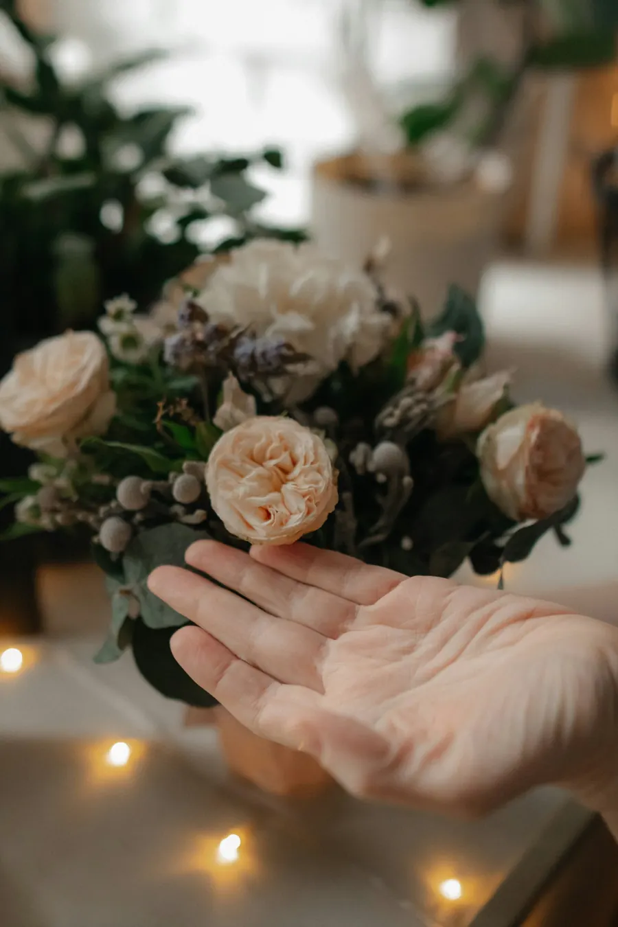 Fleuriste qui compose un centre de table de fleurs de saison, tons crème et vieux rose