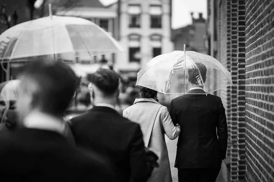 Groupe en tenue de mariage sous des parapluies transparents, rue pavée