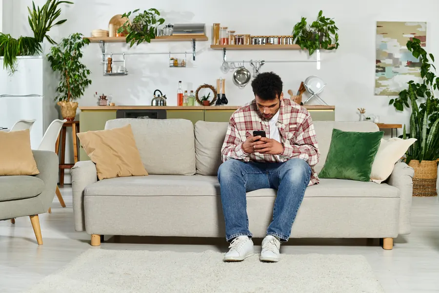 Homme cherchant un artisan sur son smartphone, dans son salon