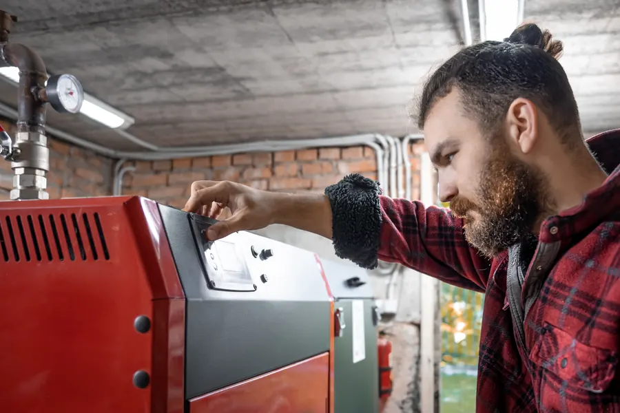 Dans une chaufferie en sous-sol, un homme règle le tableau de commande d’une chaudière à granulés rouge