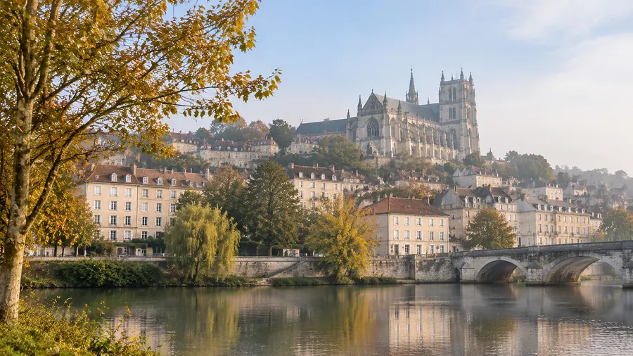 Pontoise vue des bords de l’Oise un matin d’automne : la ville en coteau, ses immeubles anciens et une grande église gothique au sommet, un pont de pierre à droite
