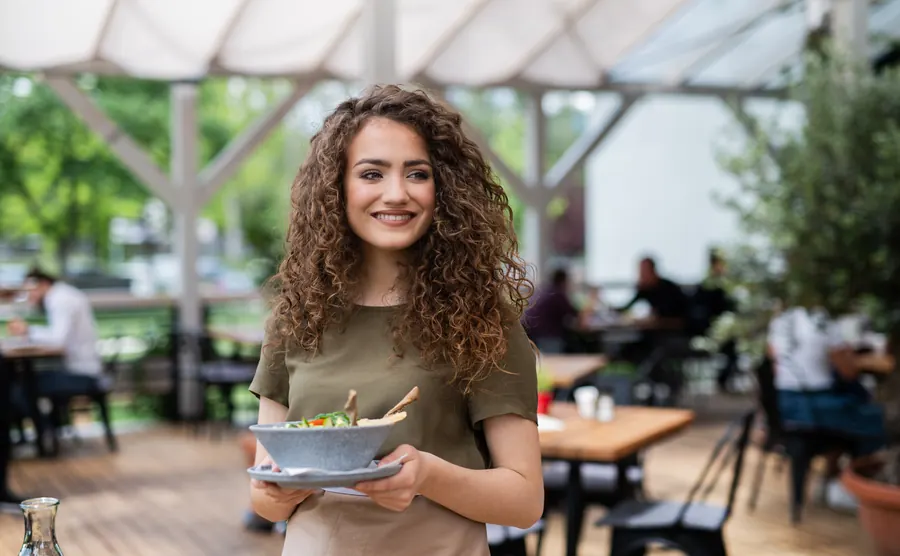 Une serveuse souriante apporte une assiette en terrasse
