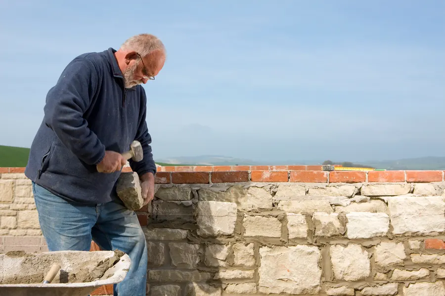 Un maçon monte un mur en pierre par une journée ensoleillée